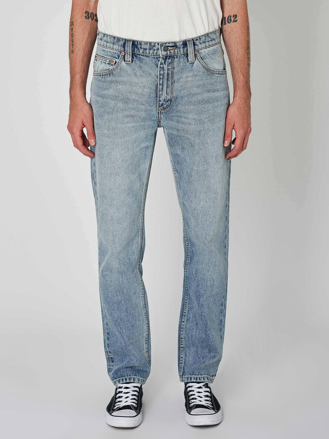 A person wears Rollas Relaxo Hemp Bleach Vintage Denim in blue, paired with black-and-white sneakers and a white T-shirt, standing front-facing against a plain light background. Only the lower body is shown.