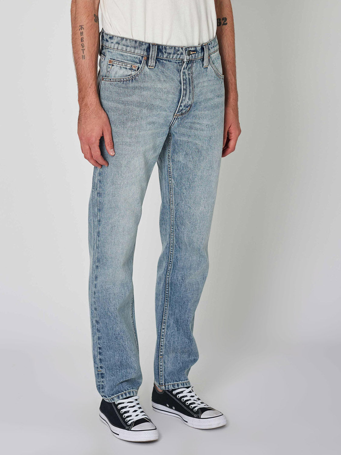 A person in Rollas Relaxo Hemp Bleach Vintage Denim, a white t-shirt, and black low-top sneakers stands against a plain light background. The face is not visible.