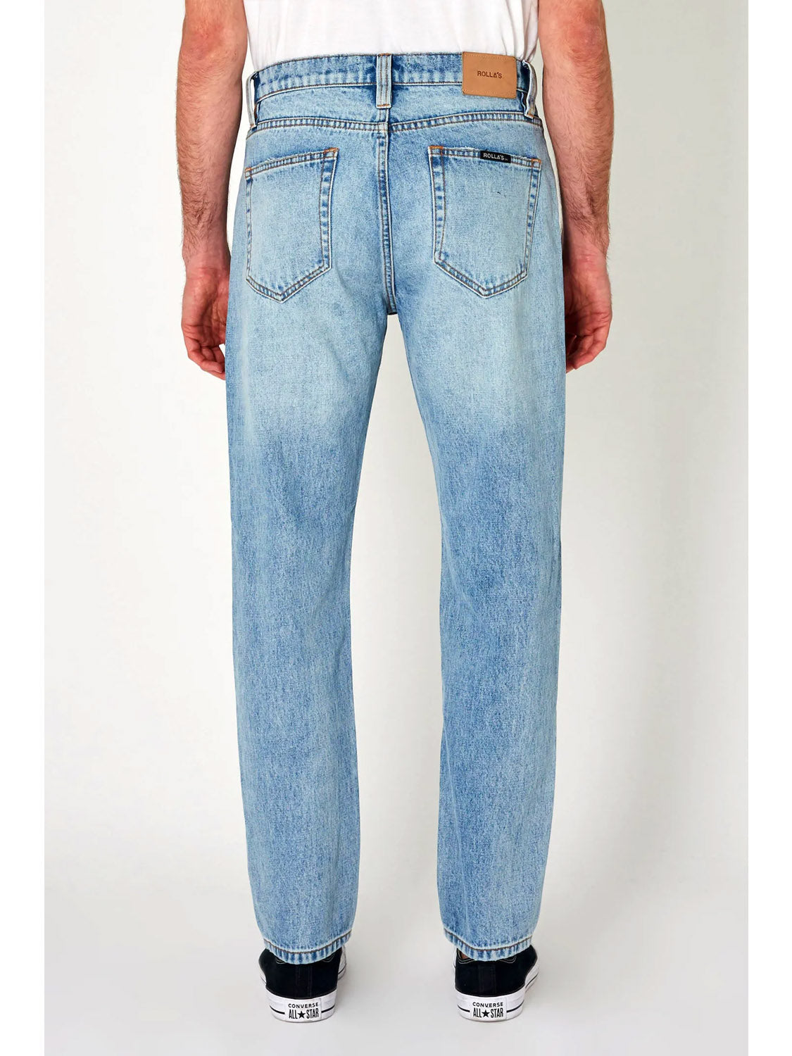 A person wearing Rollas Relaxo Original Stone Denim, a white shirt, and black sneakers stands with their back to the camera against a plain white background.