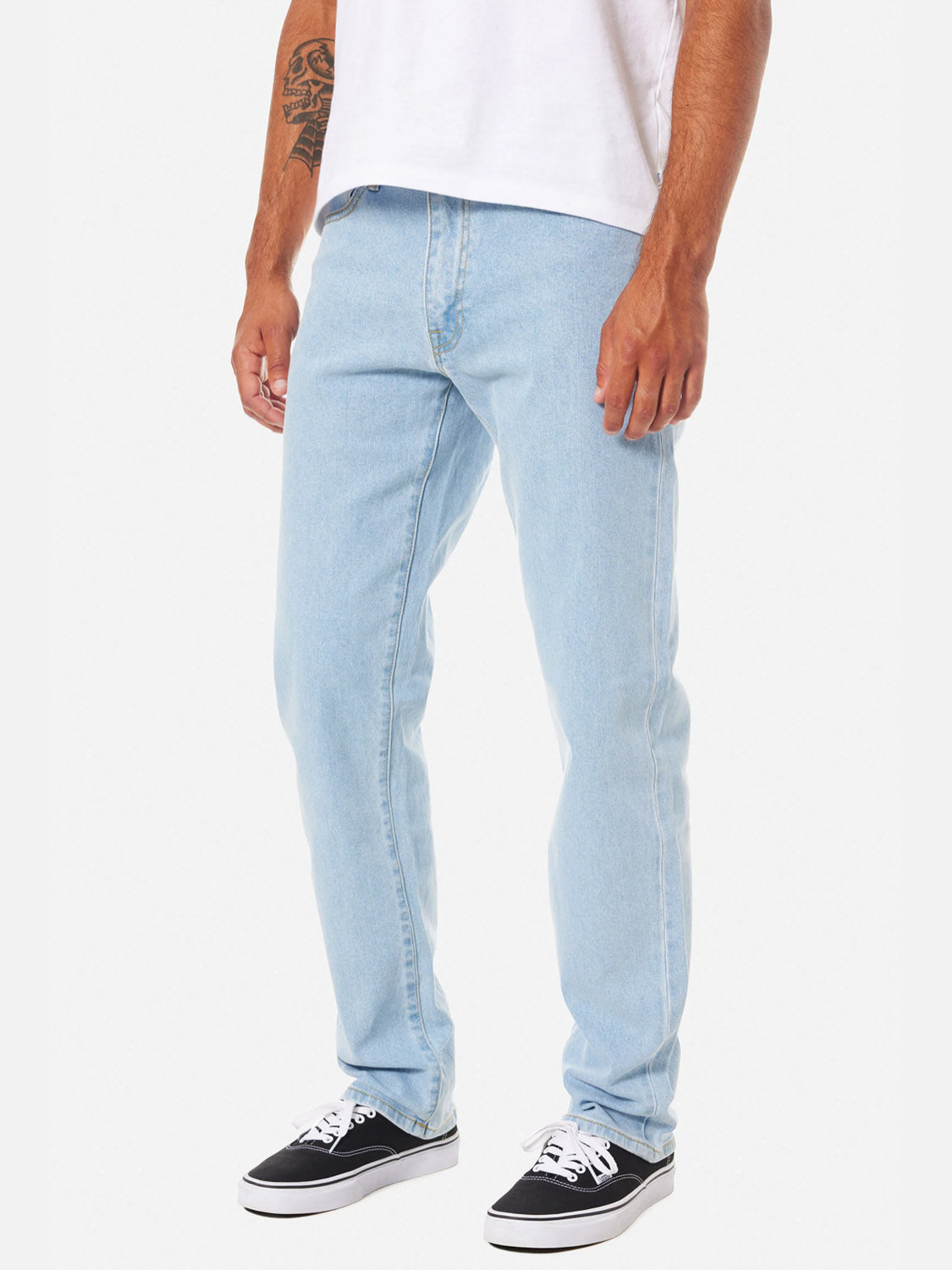 A man models the Katin Ren 57 Classic Straight Pants with 5-pocket styling, paired with a white t-shirt and black sneakers with white soles. He stands against a plain white background, showing a tattoo on his left arm. His head is not visible in the image.