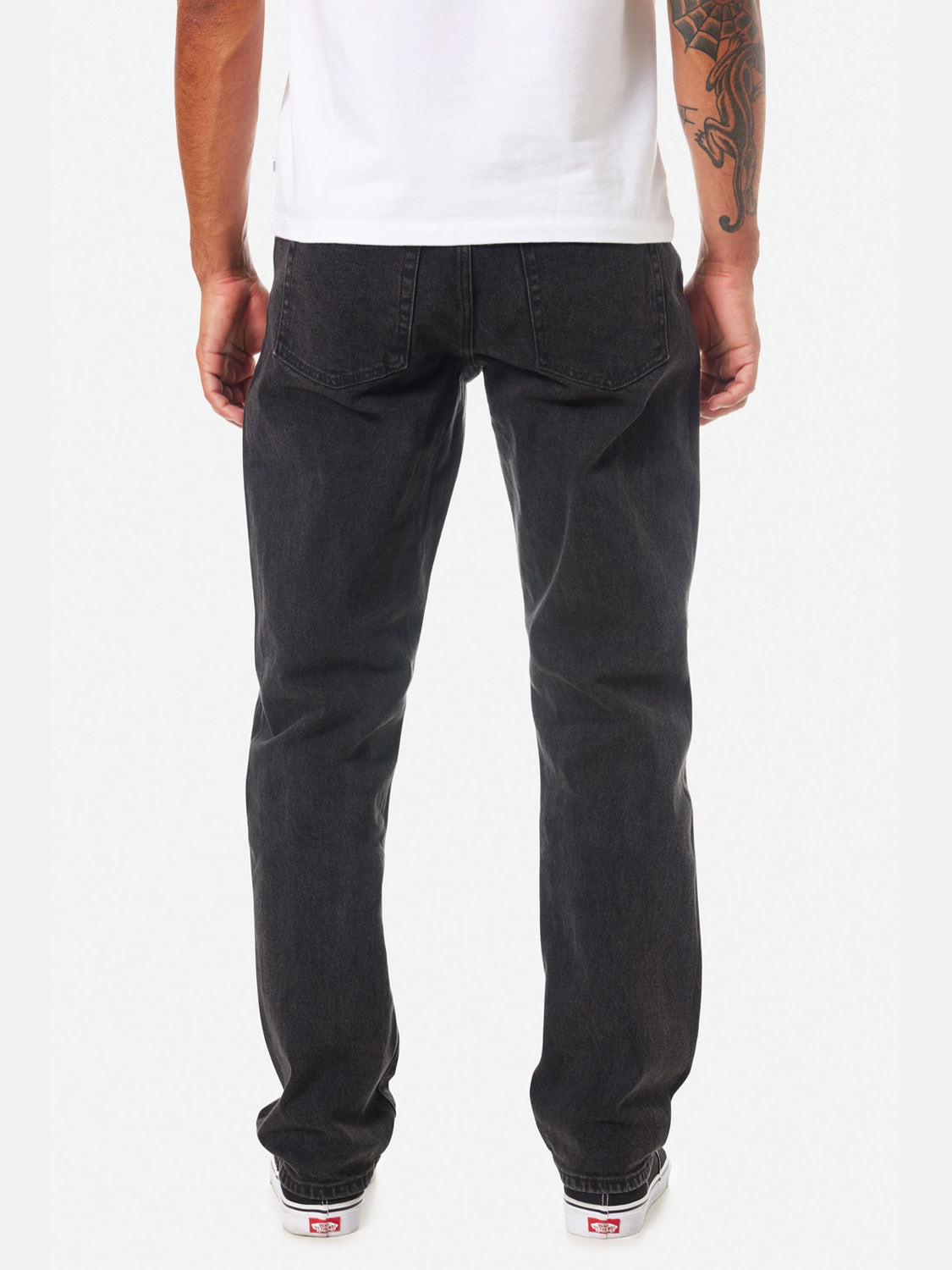 A person is shown from the back wearing a white t-shirt, white sneakers, and Katin Ren 57 Classic Straight Pants in black denim with 5-pocket styling. They have a tattoo on their right forearm. The background is plain white.