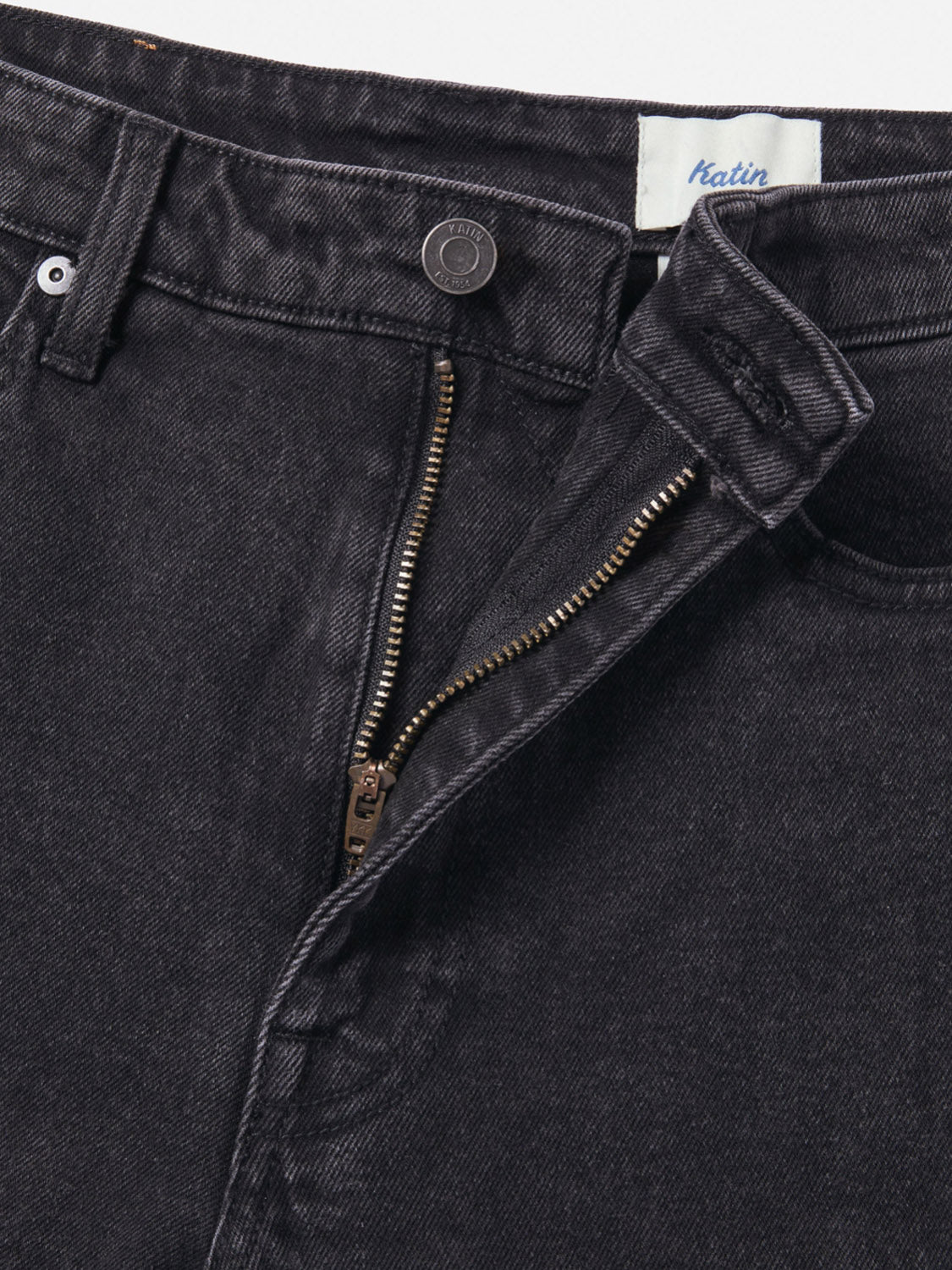 Close-up of Katin Ren 57 Classic Straight Pants in black denim, featuring a partially unzipped fly with metal zipper, button closure, belt loops, 5-pocket design, and visible waistband label.