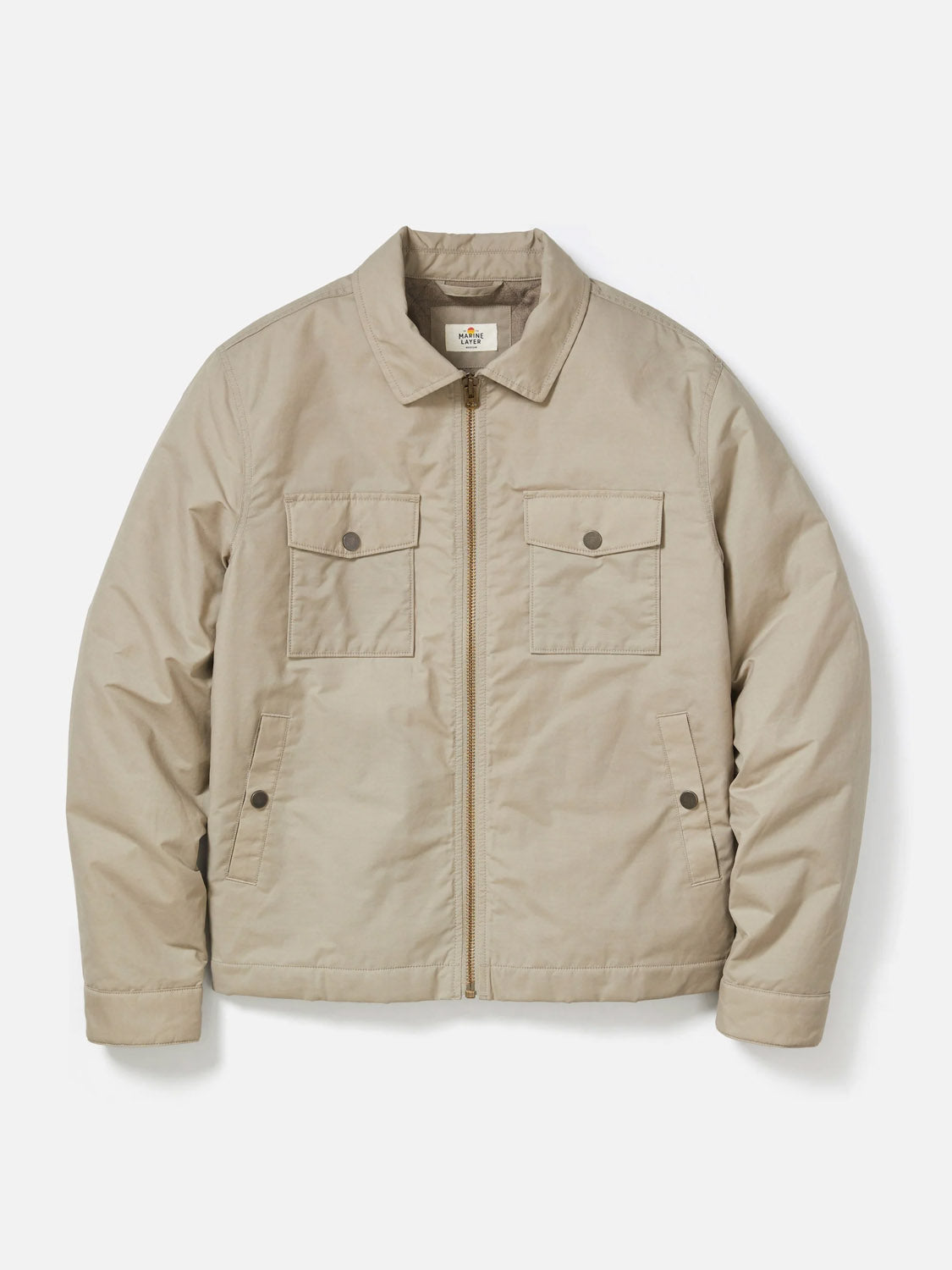 The Marine Layer Reynolds Dry Wax Trucker Jacket is a light beige, long-sleeve workwear style with a collar and two buttoned chest pockets, shown flat on a white background.