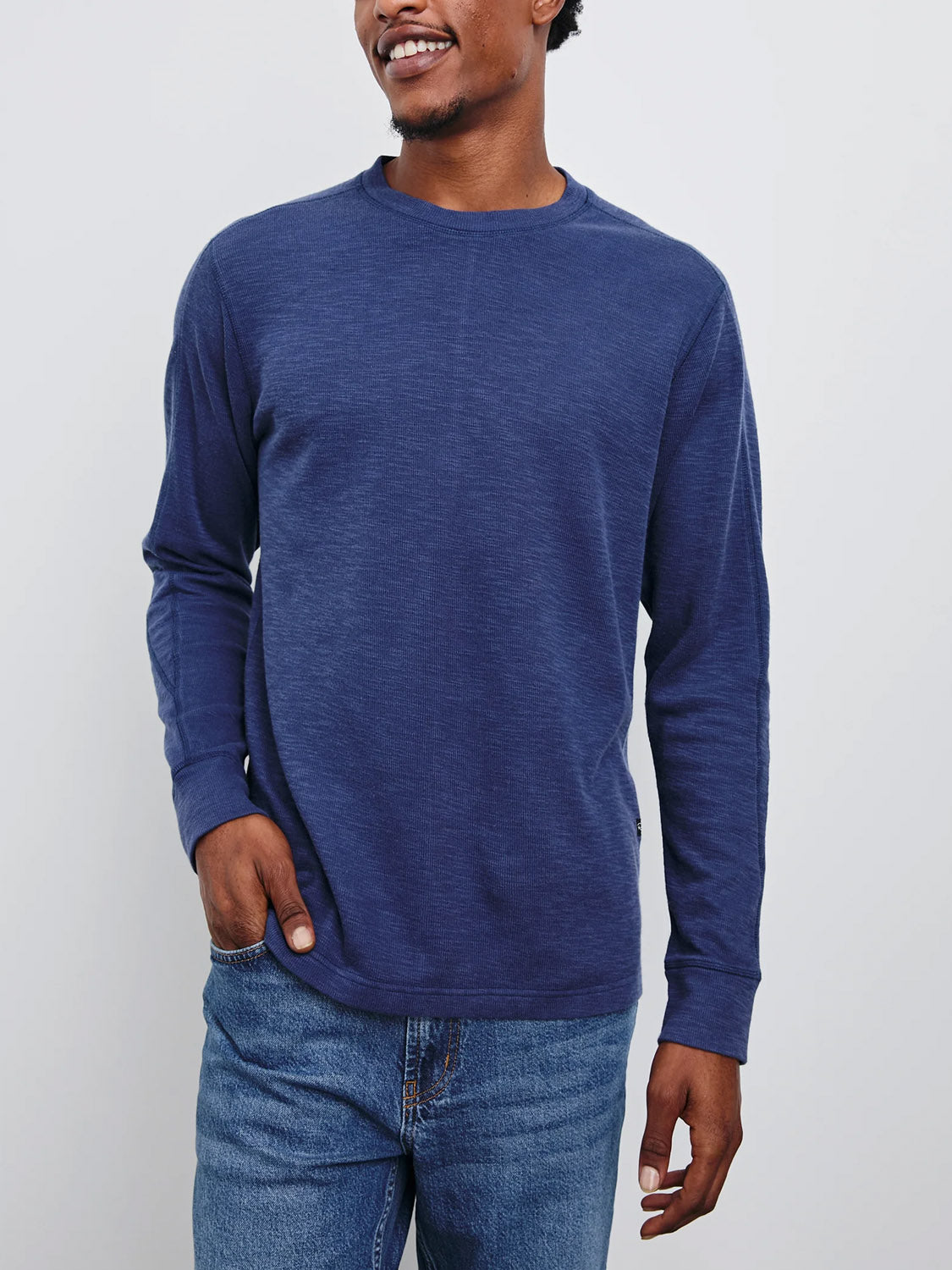 A person wearing a Rails Rheese Long Sleeve Thermal and jeans stands against a plain white background, smiling with one hand in their pocket.