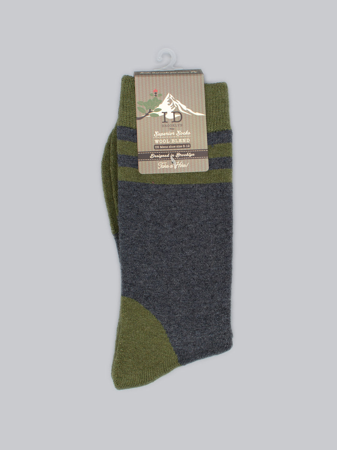 A pair of green and gray Rockies Merino Wool Socks by ID Menswear with a rustic cardboard label featuring a mountain silhouette and decorative text emphasizing warmth, comfort, and durability.