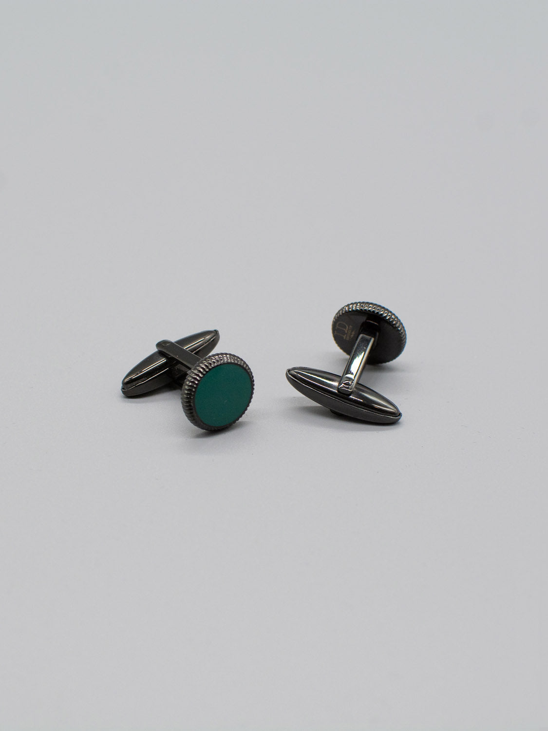 The ID Menswear Black Gold Plated Steel Enamel Cufflinks, featuring green circular enamel inlays, rest on a plain light gray surface, showcasing their simple and elegant design.