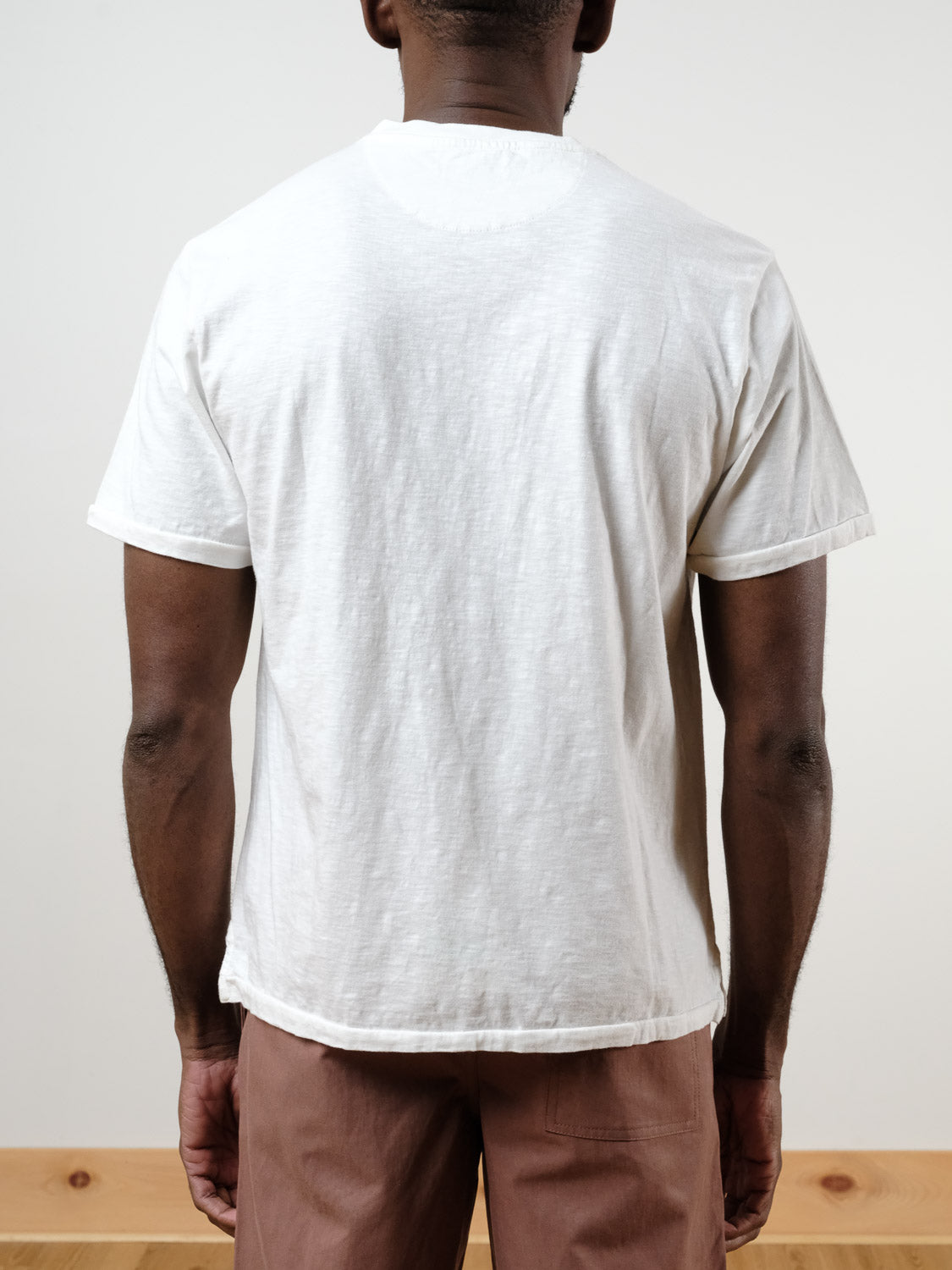 A person stands indoors with their back to the camera, wearing the Rogue Henley by ID Menswear and light brown pants. The setting features a neutral background and wooden floor.