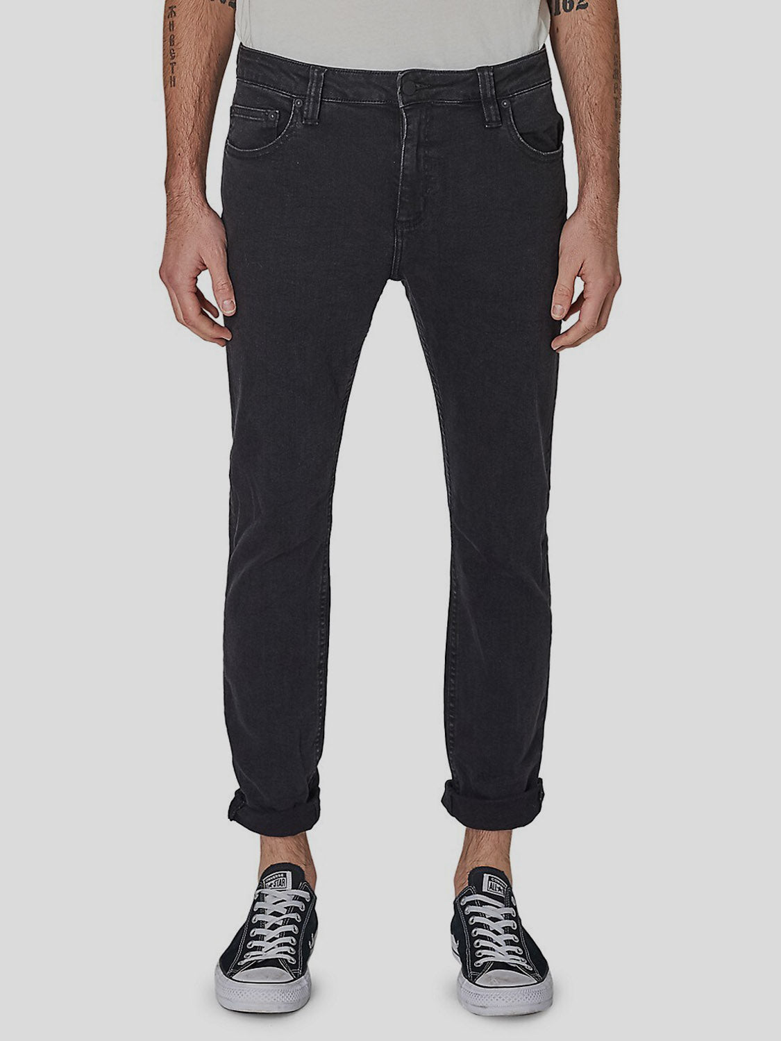 Wearing Rollas Rollies Slim Fit Jean with rolled-up cuffs and black-and-white sneakers, a person stands against a plain light gray background, showing only the lower half of their body.