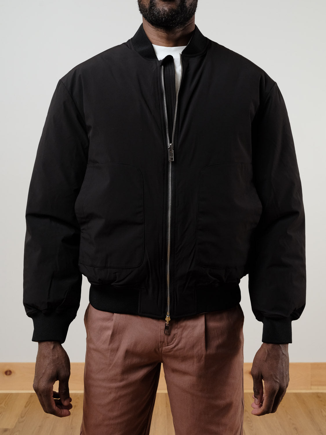 A man stands against a plain background, hands relaxed by his sides, wearing the !SOLID Romeo Reversible Bomber Jacket in black over a white shirt and light brown pants.