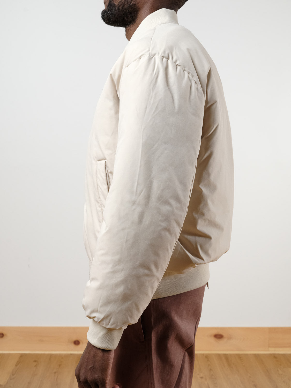 A person models the !SOLID Romeo Reversible Bomber Jacket in light beige with brown pants, standing sideways against a plain background, showing only their upper body.