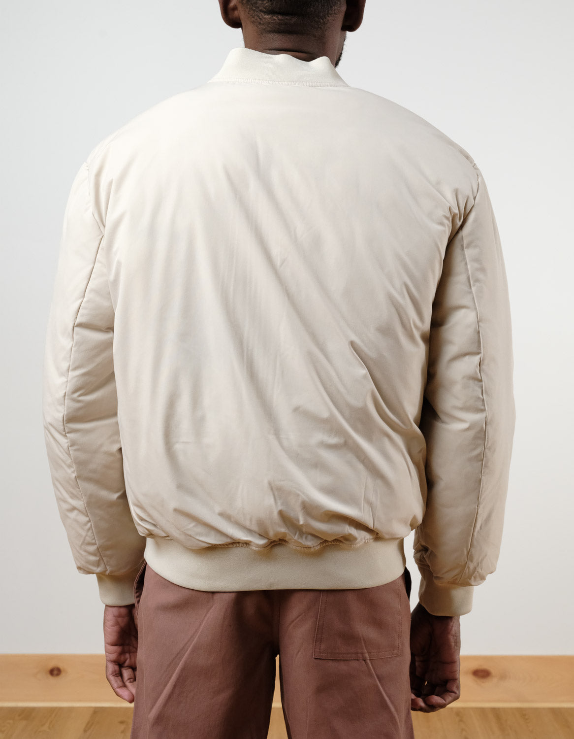 A person stands indoors facing away, wearing the !SOLID Romeo Reversible Bomber Jacket in light beige paired with light brown pants against a plain background.