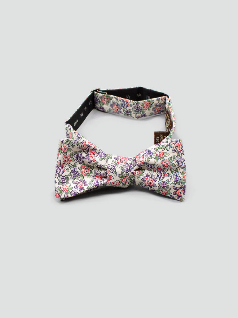 The Liberty of London Tana Lawn™ Rosey bow tie by ID Menswear is handmade from colorful floral cotton in pink, purple, and green on white, shown against a light gray background.