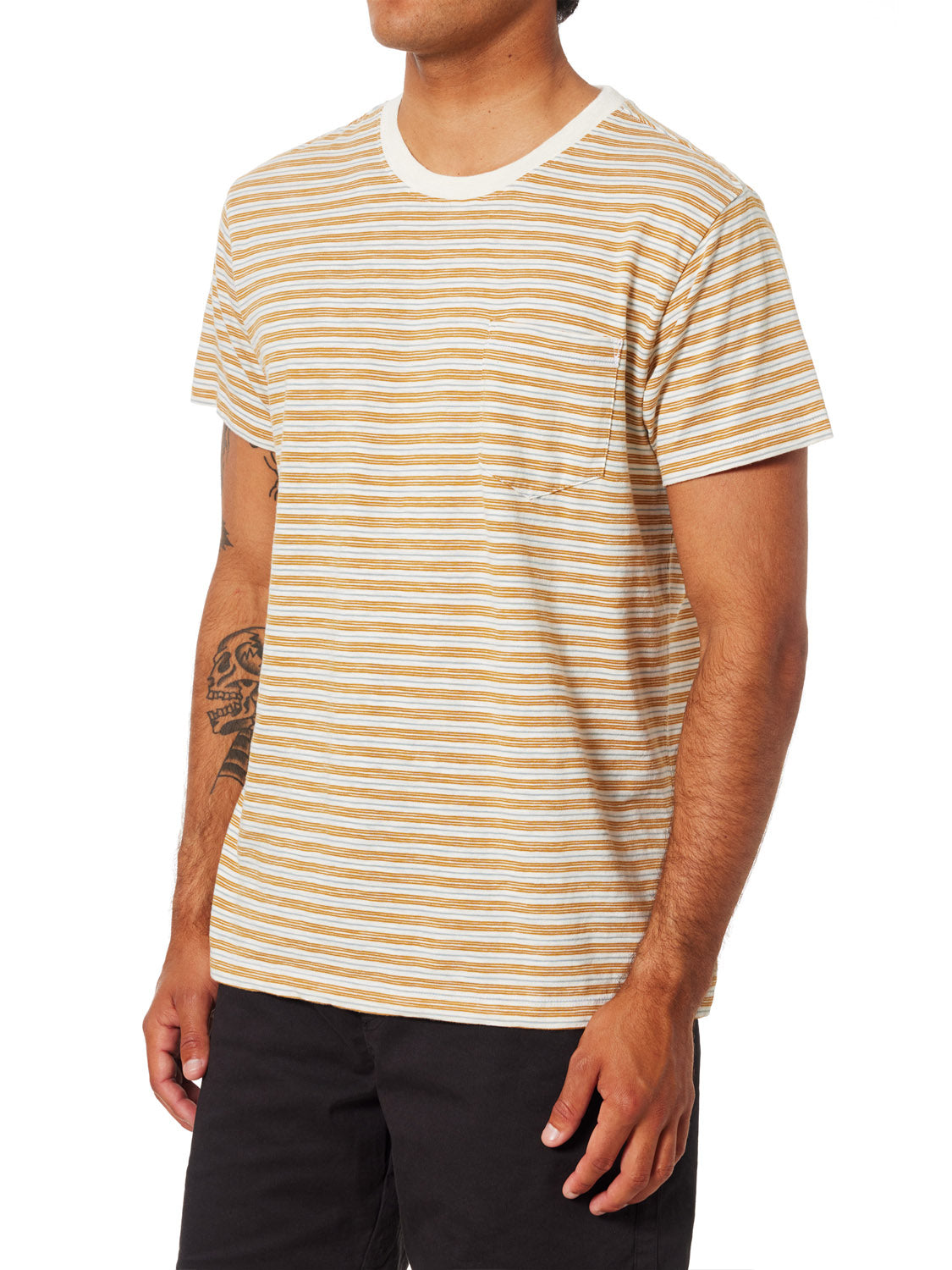 A person is wearing a Katin Rural Pocket Tee, featuring short sleeves and tan and white stripes in premium cotton, paired with black pants. They display a tattoo on their left forearm while standing against a plain white background.
