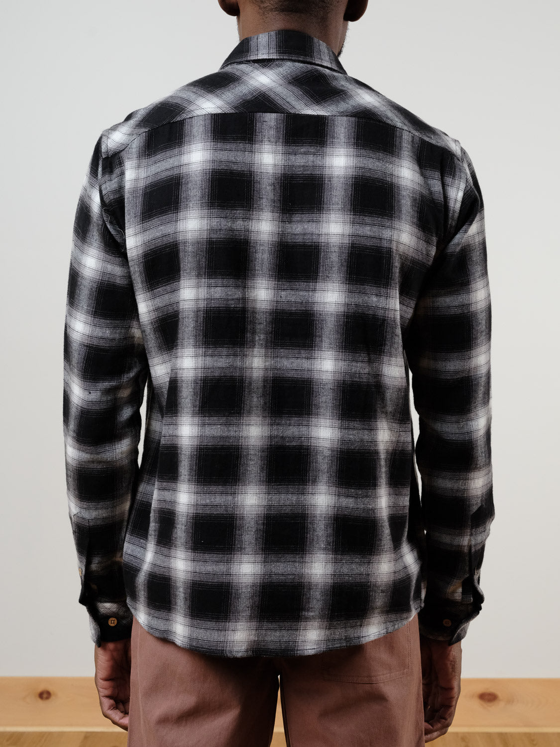 A person stands with their back to the camera, wearing the !SOLID Rye Organic Cotton Plaid Button-Down Shirt in black and white, paired with light brown pants against a plain light background.