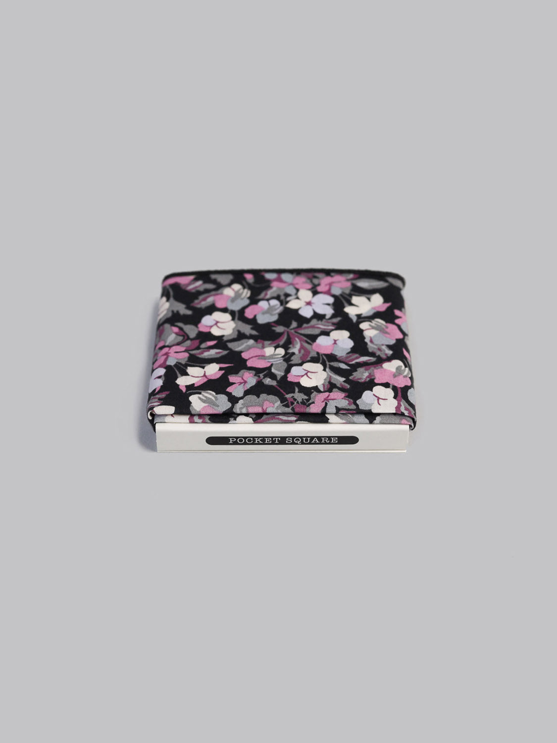 The Liberty™ Sarah P. Pocket Square by ID Menswear features a black background with white, pink, and gray florals, folded with a silver POCKET SQUARE clasp on a light gray surface—handmade in Brooklyn.