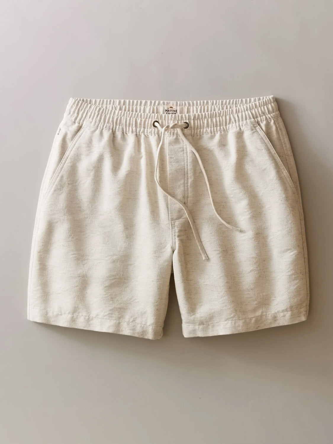 Marine Layer Saturday Beach Short 6": Cream-colored jacquard shorts with an elastic waistband and side pockets, featuring a subtle leaf texture, displayed on a neutral background.