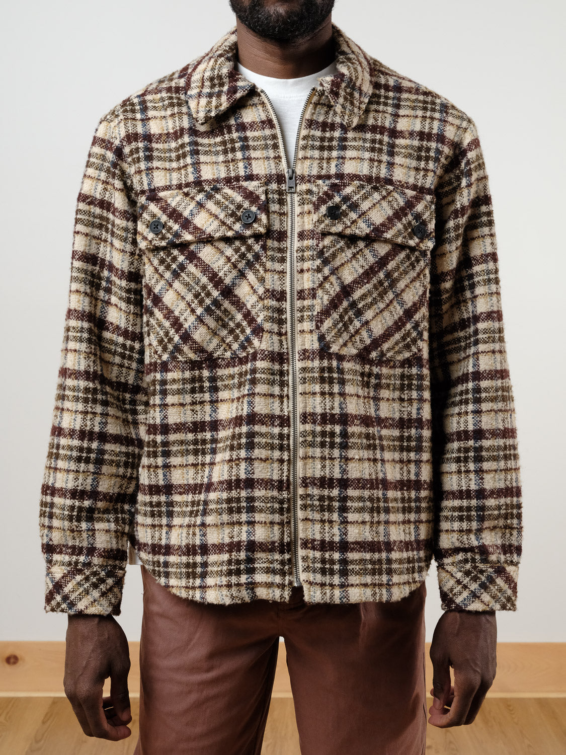 A person wears the !SOLID Sclade Box Fit Plaid Zip Shacket in beige, brown, and black with chest pockets over a white shirt and brown pants, standing against a plain light background.