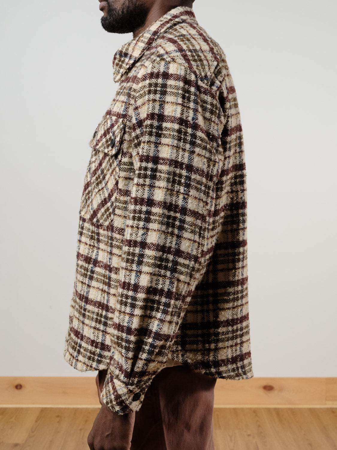 A person stands in profile against a light background wearing the !SOLID Sclade Box Fit Plaid Zip Shacket in beige, brown, and black plaid with chest pockets, paired with brown pants.