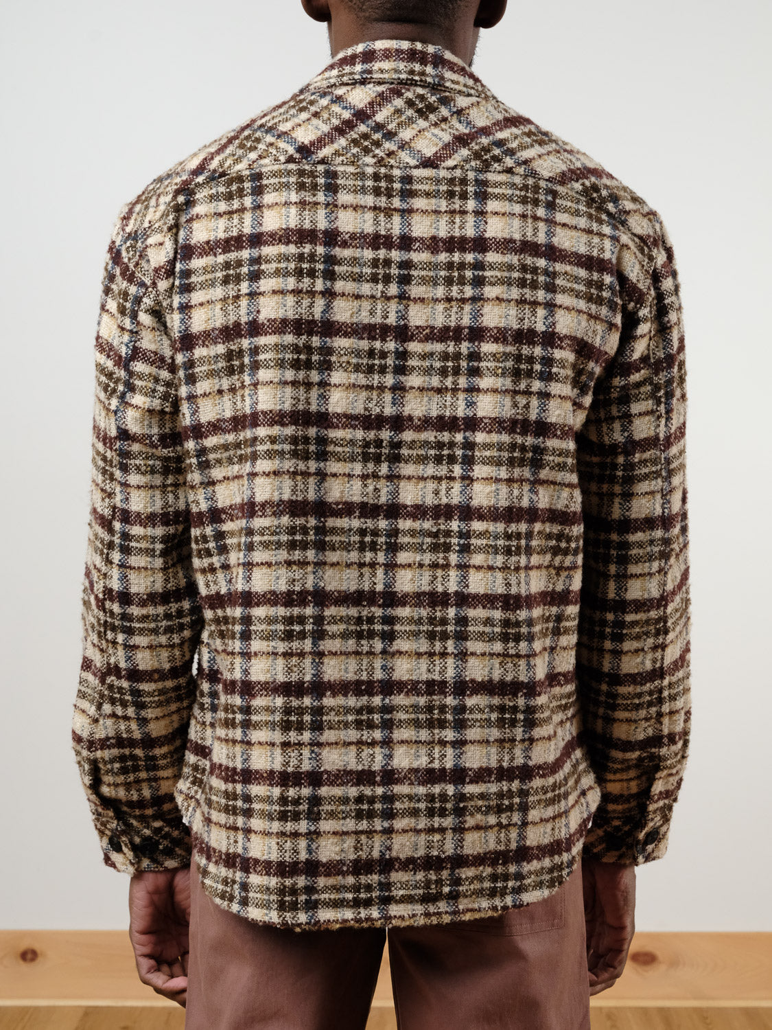 A person faces away from the camera wearing the !SOLID Sclade Box Fit Plaid Zip Shacket in beige, brown, and black with long sleeves, paired with brown pants. The background is plain and light-colored.