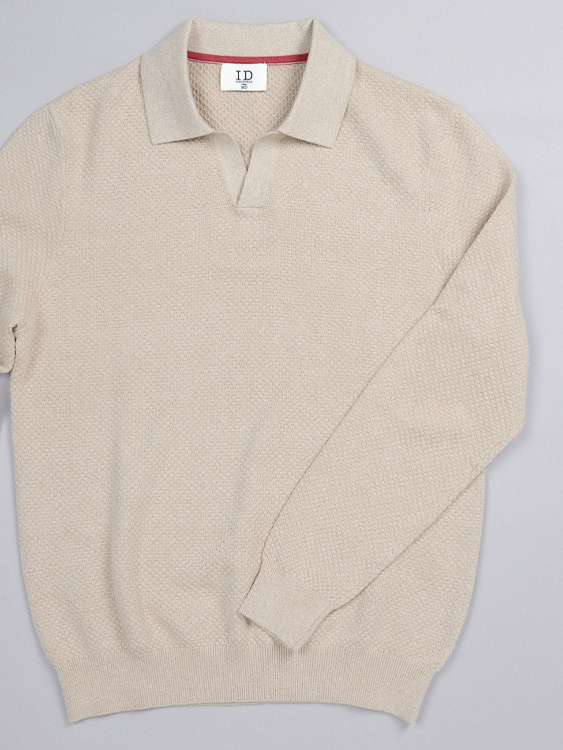 The Seattle Long Sleeve Cotton Polo by ID Menswear is a beige knit sweater with a collar and subtle texture, ideal for smart-casual occasions. Laid flat on a gray background, the collar tag reads ID, adding a personal touch.