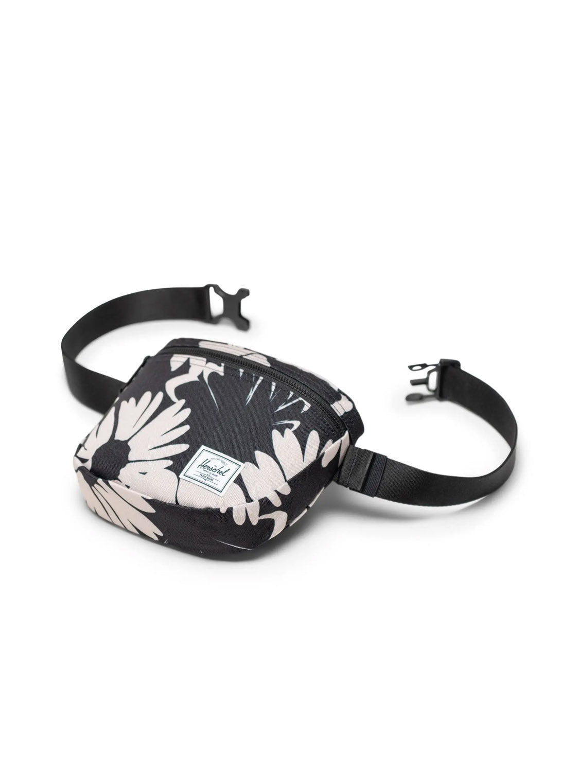 The Herschel Settlement Hip Pack - 2L is a black and white floral-printed hip pack made from recycled polyester, featuring an adjustable strap, front pocket with brand label, and is perfect for hands-free travel. Displayed on a white background.