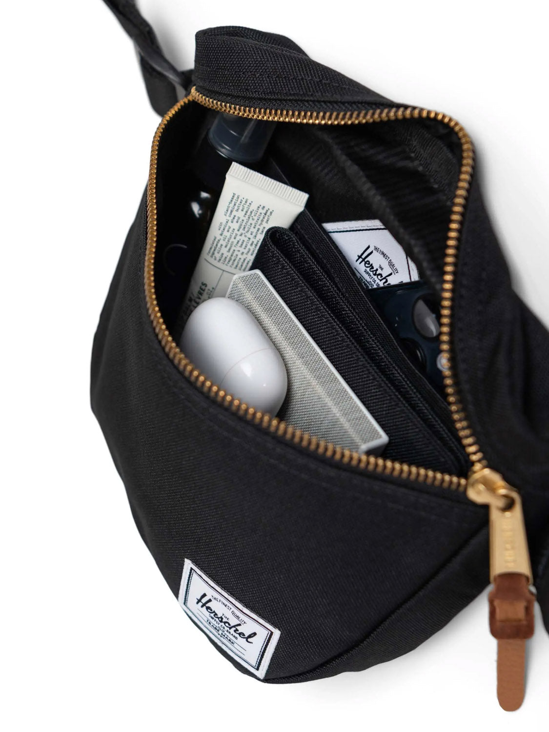 The Herschel Settlement Hip Pack - 2L, shown open against a white background, features recycled polyester material and neatly stores essentials like a cardholder, small bottles, and earbuds—ideal for hands-free convenience.