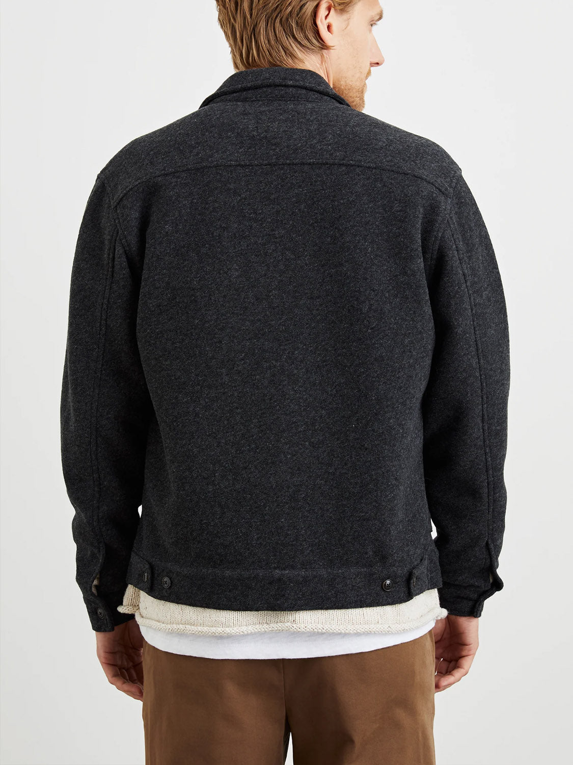 A man with light brown hair is shown from the back, wearing the Rails Shael Jacket in dark gray wool boucle over a white shirt and tan pants, standing against a plain white background.