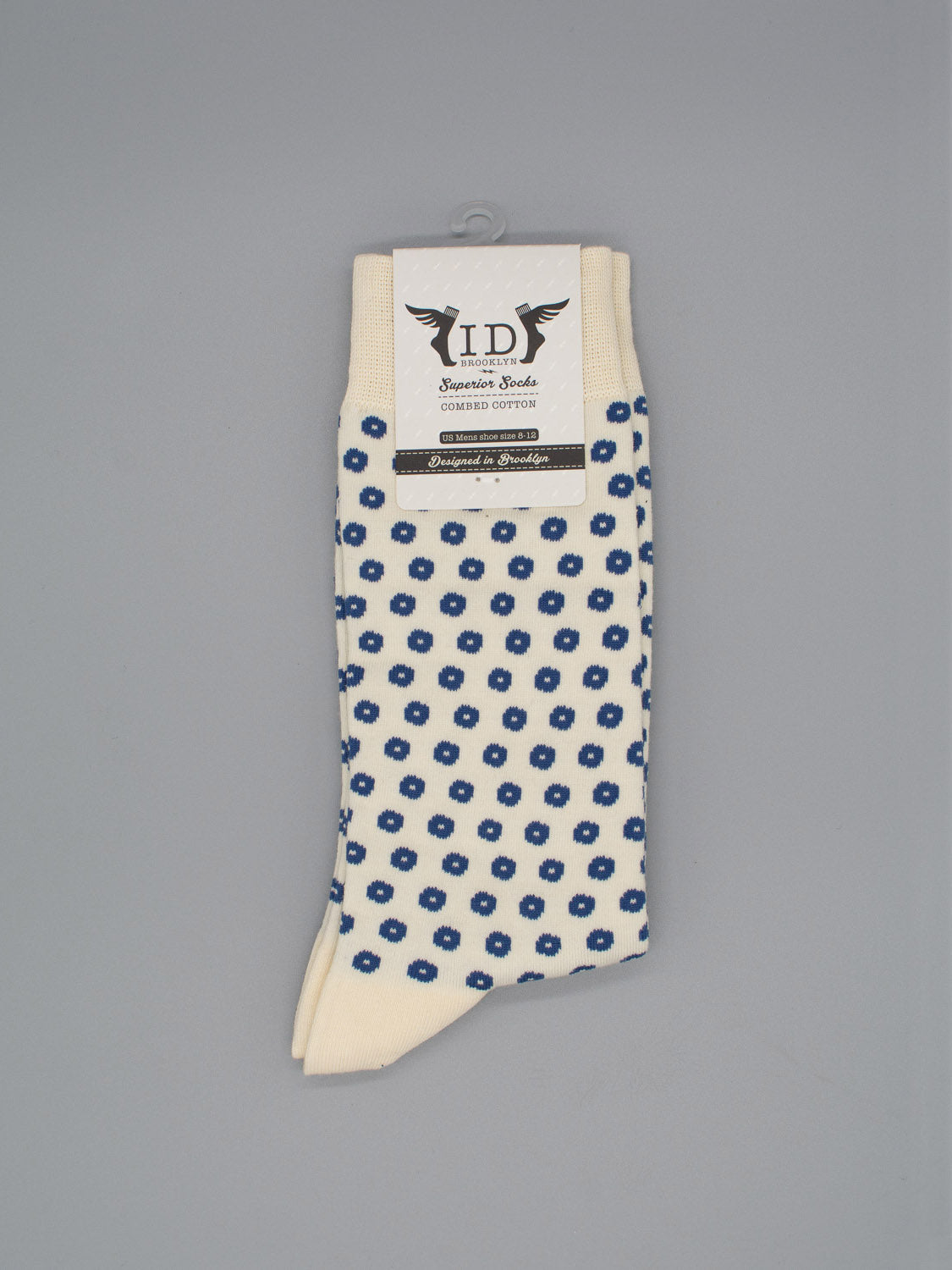 The Shibori Graphic Socks by ID Menswear are cream-colored, featuring a small blue floral pattern, made from soft combed cotton, and shown folded with a label on a gray background.