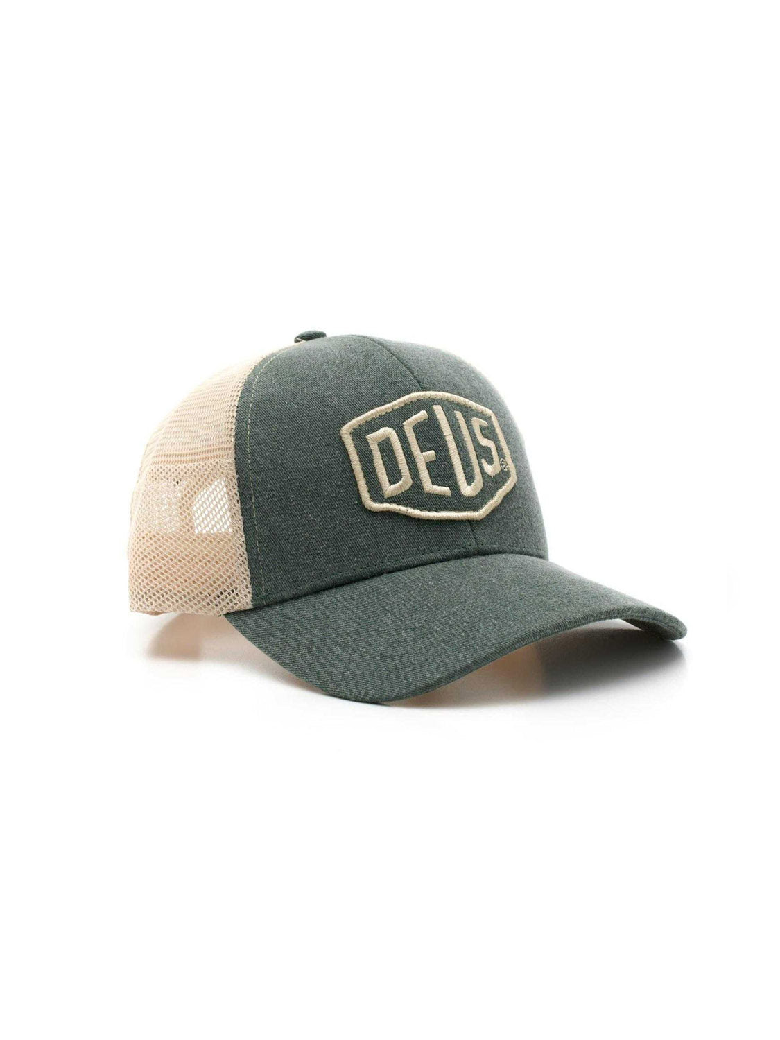 The Deus Shield Trucker is a green and beige cotton canvas hat with a mesh back, curved brim, snapback closure, and a large embroidered DEUS patch on the front. Shown photographed on a white background.