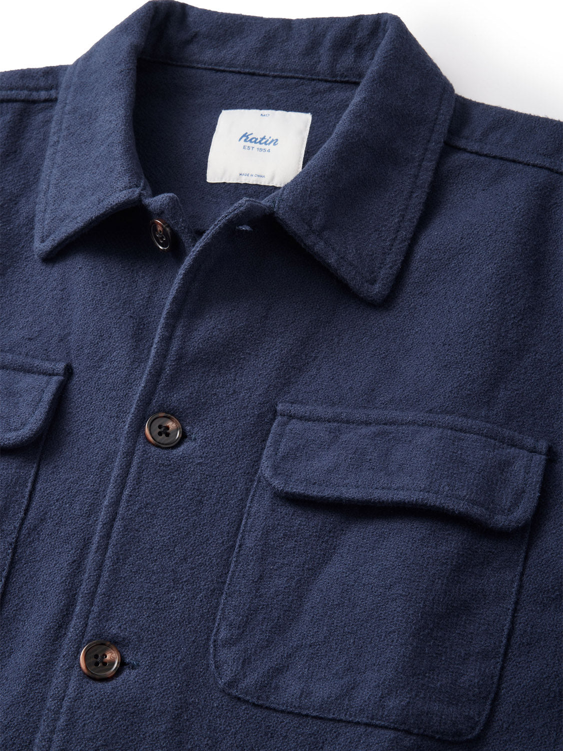 A close-up of the Katin Shiloh Solid Flannel Shirt, featuring navy heavyweight textured cotton flannel, two chest pockets, brown buttons, and a white label inside the collar.