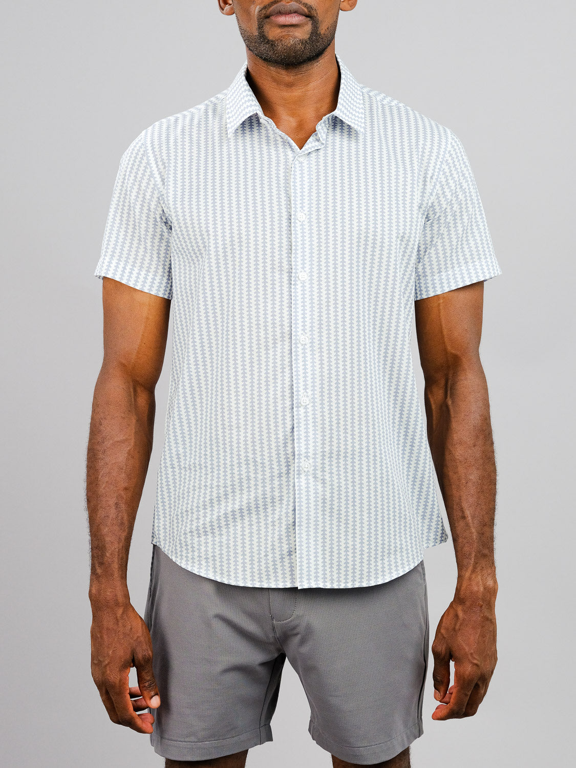 A man wears the Shima Printed Cotton Shirt by ID Menswear with gray shorts, standing against a plain light gray background with his arms relaxed at his sides.