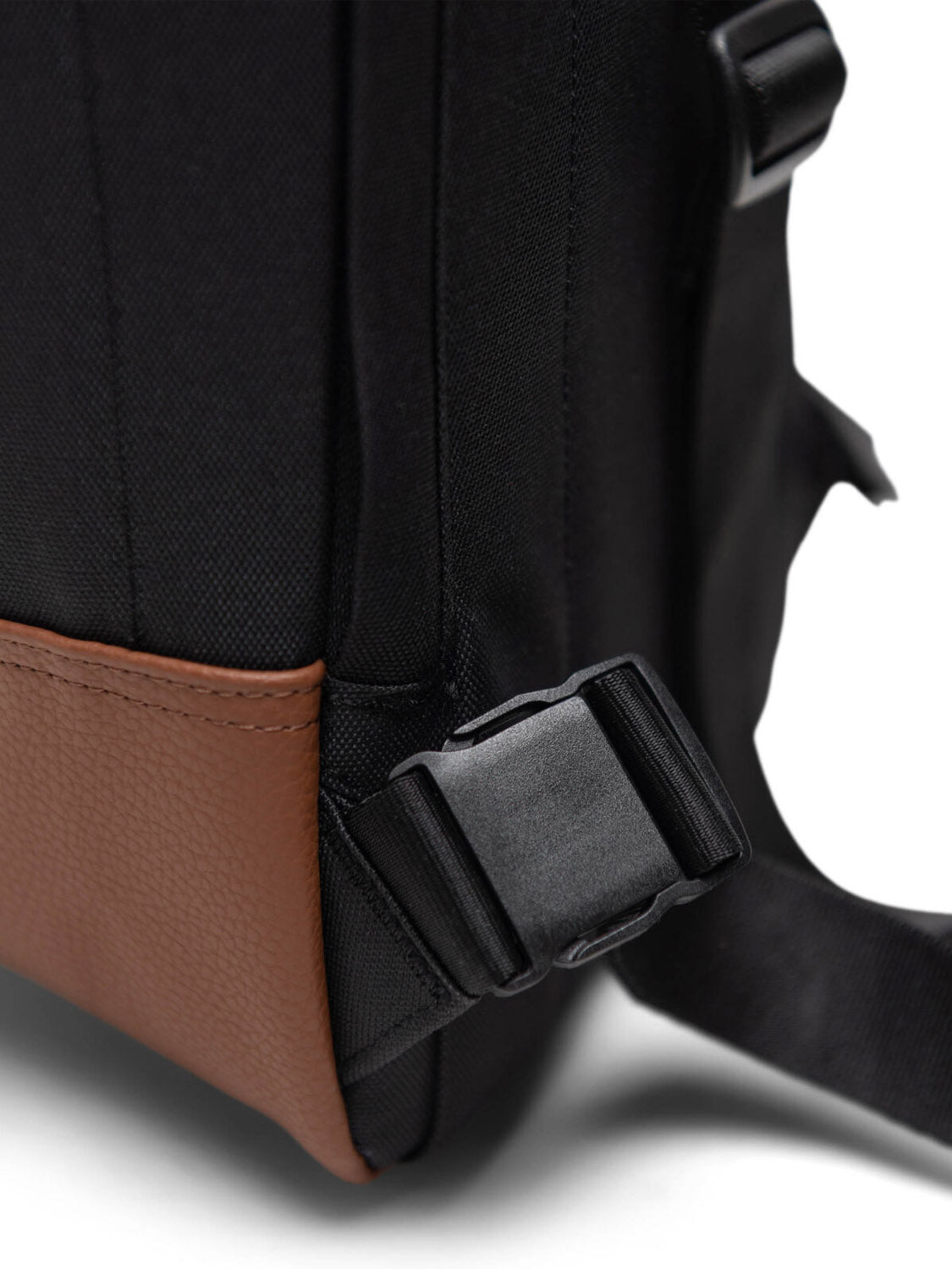 Close-up of the Herschel Heritage Shoulder Bag, featuring a black adjustable strap with plastic buckle, black fabric, and a brown textured leather bottom panel.