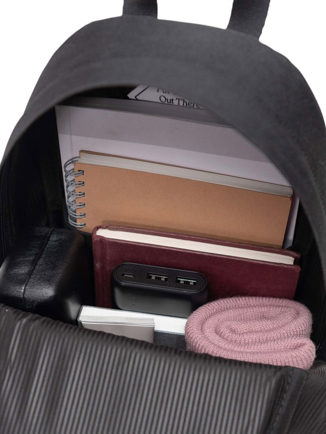 A Herschel Heritage Shoulder Bag in black sits open, revealing books, a spiral notebook, a power bank, a rolled-up pink scarf, and a small black pouch.
