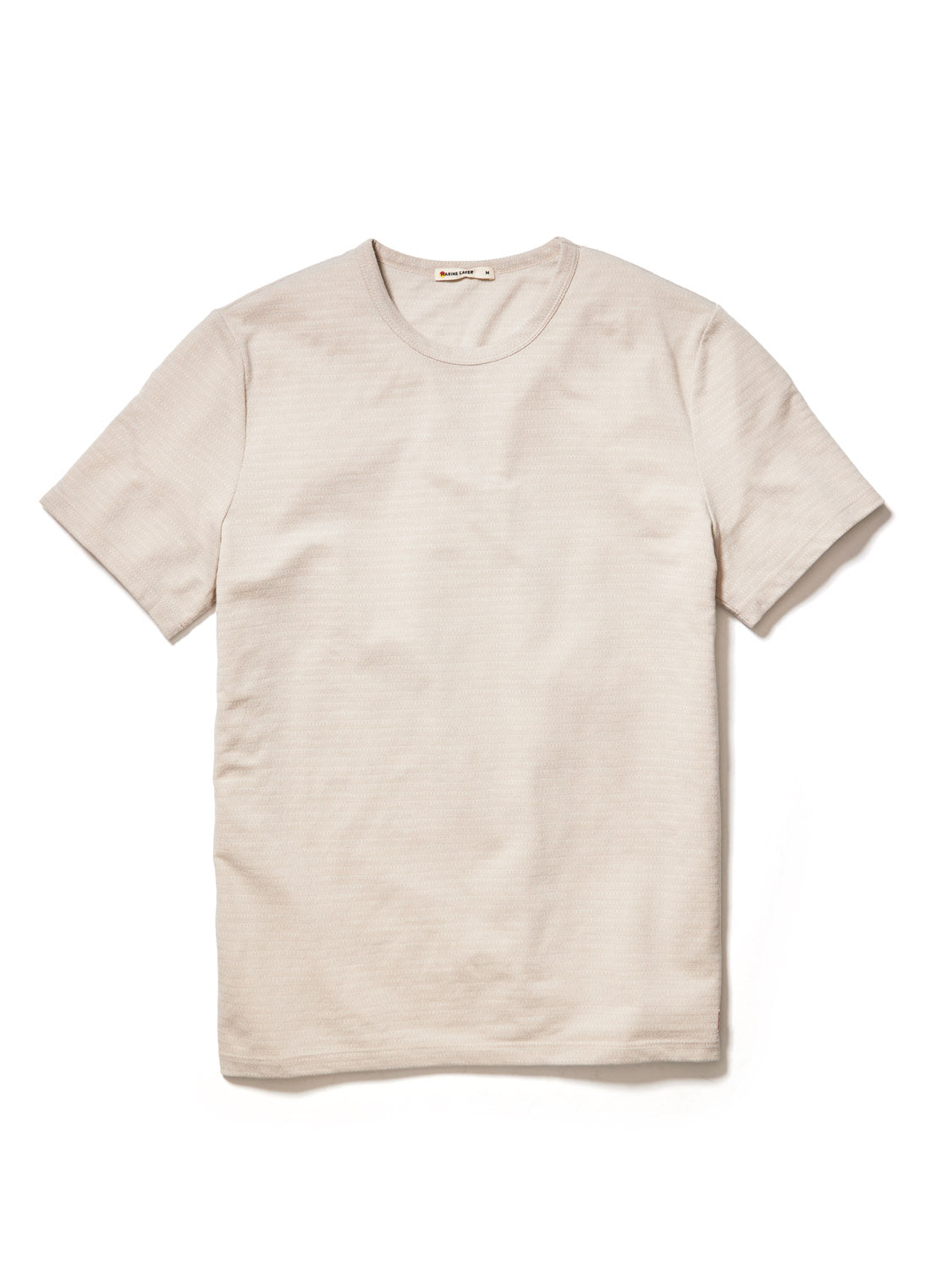 The Marine Layer Signature Jacquard Crew Tee is showcased on a white background. This light beige, eco-friendly shirt features a round neckline and textured jacquard fabric, crafted from recycled polyester. Its short-sleeved and free of visible logos or patterns.