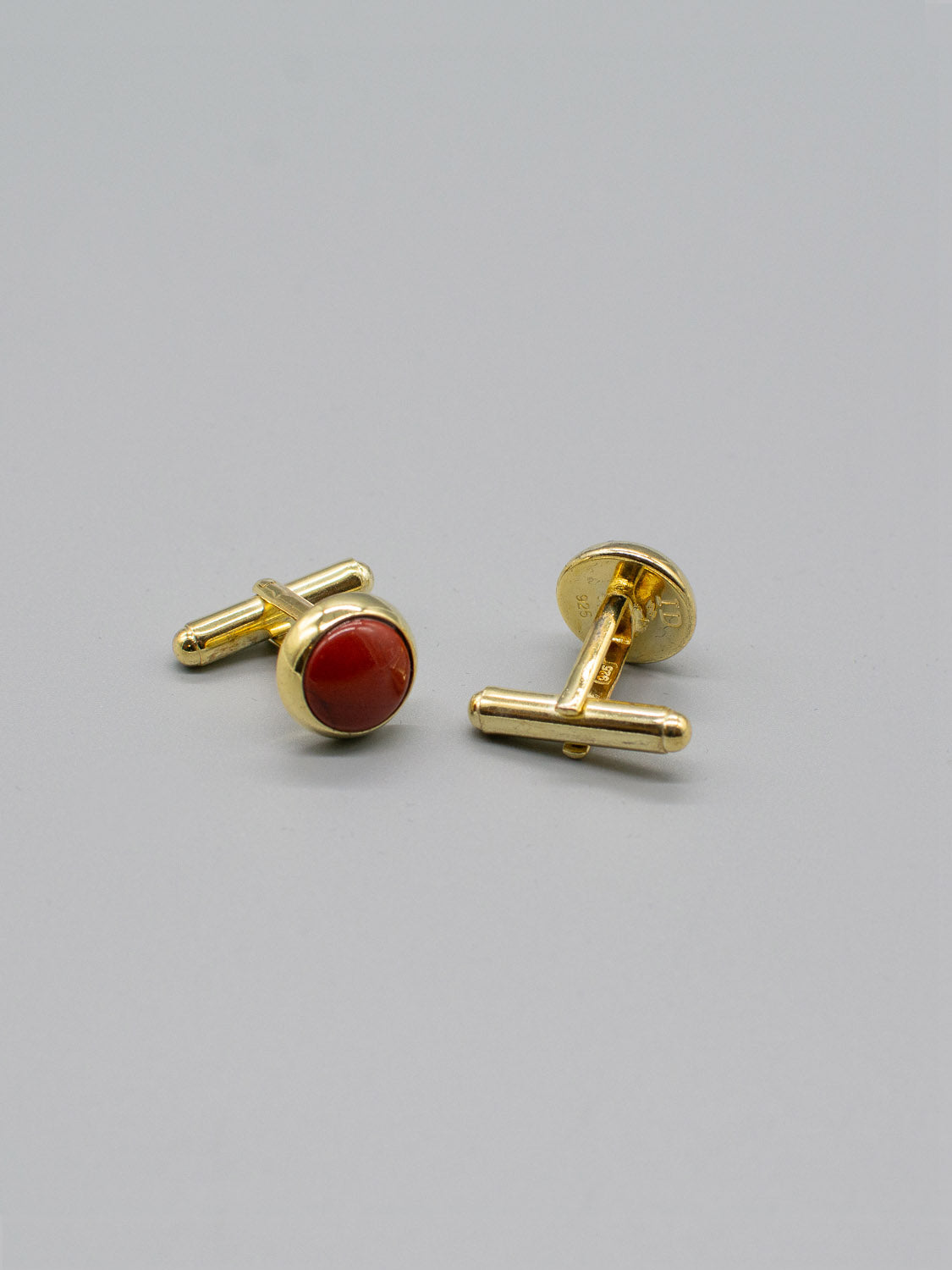 ID Menswears Gold Plated Silver Gemstone Cufflink set is displayed on a plain background. One cufflink shows off its round red gemstone inlay, while the other reveals the bullet back mechanism, both artfully angled for effect.