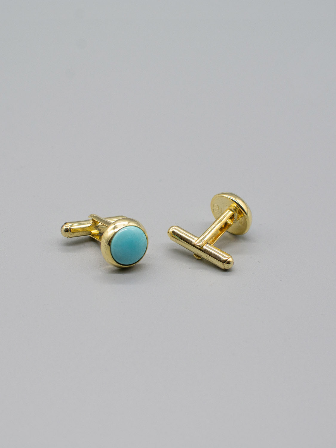 Two ID Menswear Gold Plated Silver Gemstone Cufflinks are showcased on a neutral background. One reveals a round turquoise gemstone inlay, and the other highlights its T-bar closure with a bullet back mechanism. Both feature a shiny, polished finish.