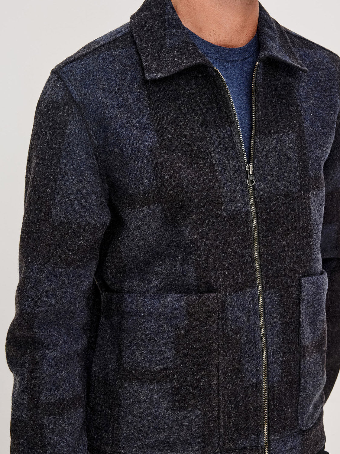 A man facing forward, shown from shoulders to waist, wears the Rails Simon Jacket—a dark plaid wool blend zip-up—over a blue shirt.