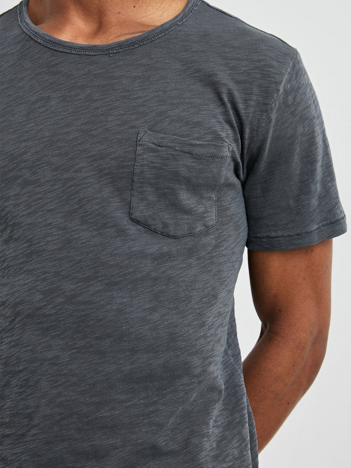 A person in a dark gray Rails Skipper Tee with a vintage wash and small chest pocket stands against a plain background. Made of super soft cotton, the short-sleeve tee allows their arms to relax at their sides, while their head remains out of frame.