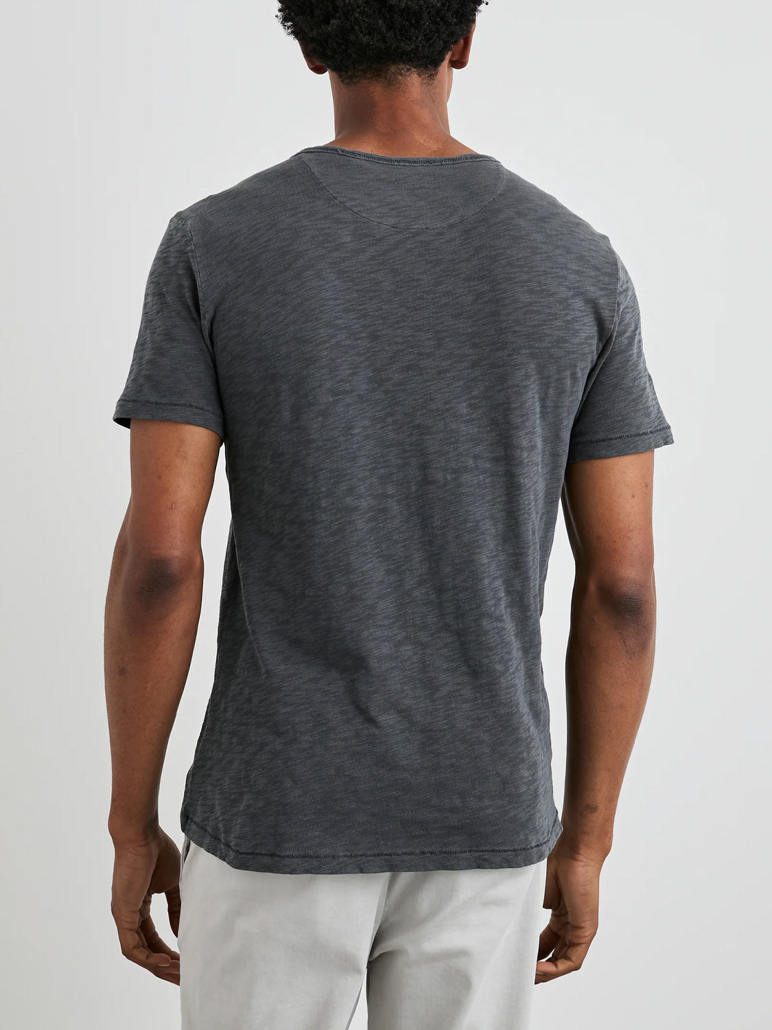 A person wearing the Rails Skipper Tee, a gray, short-sleeve T-shirt by Rails made from super soft cotton with a vintage wash effect, paired with light-colored pants. The plain, light-colored background emphasizes the T-shirts casual and relaxed fit.