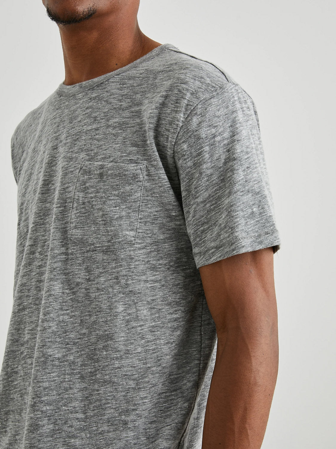A person wearing the Rails Skipper Tee, a gray marled short-sleeve shirt by Rails with a vintage wash and small chest pocket, stands against a neutral background. The image highlights the upper body with part of the face and arm visible.