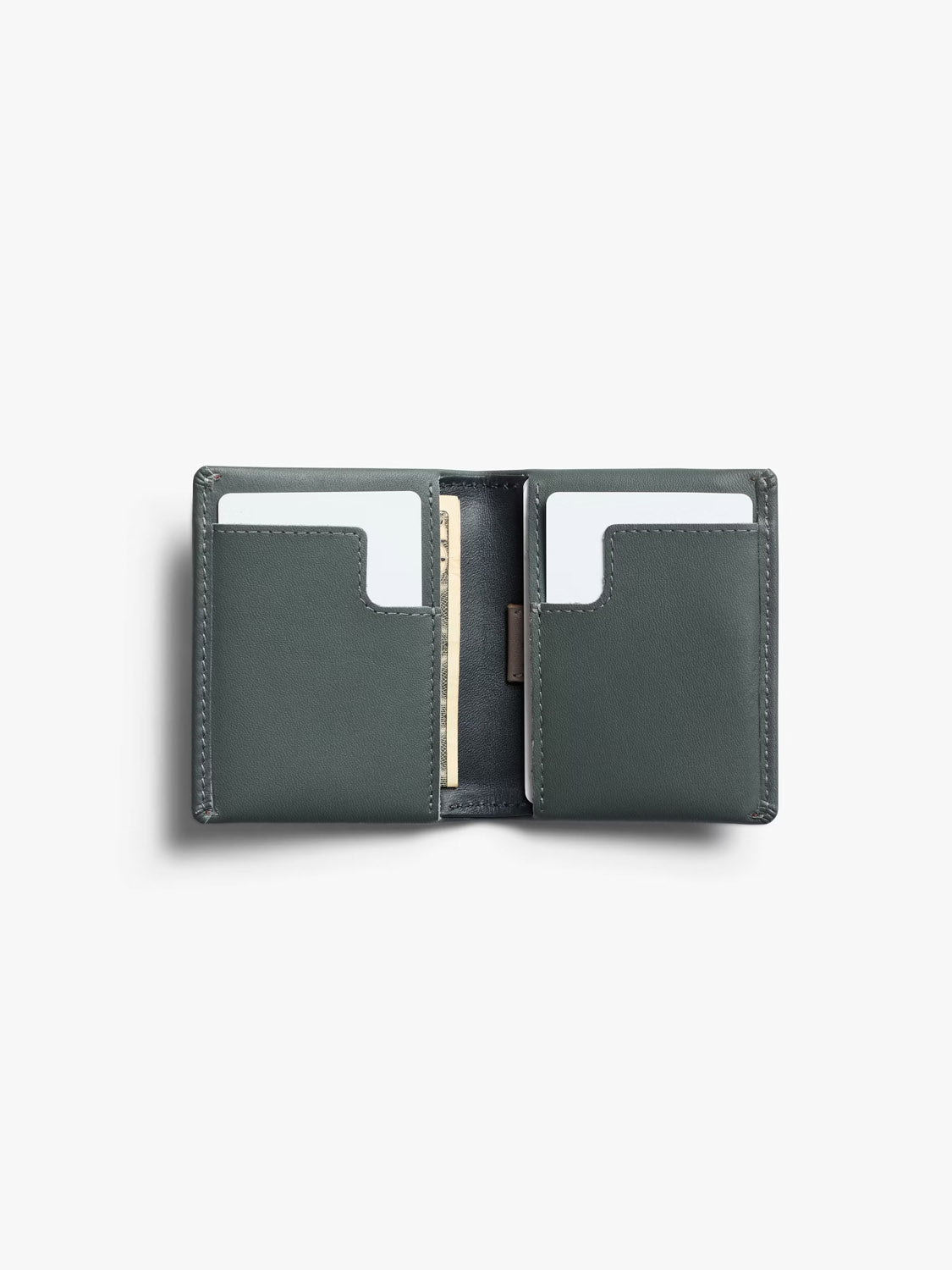 The Bellroy Slim Sleeve Wallet in dark green leather is shown open on a plain white background, displaying two white cards in its card slots and a folded bill tucked into the center section.
