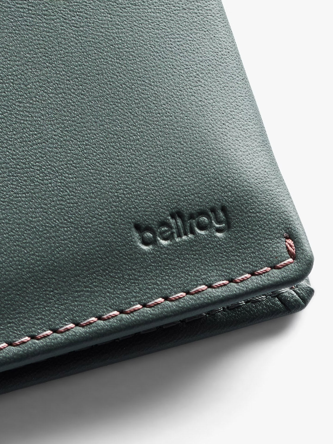 Close-up of a dark green Bellroy Slim Sleeve Wallet corner, showing pink stitching and the embossed brand—a stylish slim wallet and card holder in one.