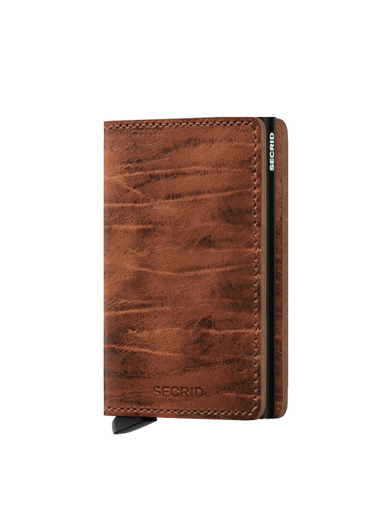A Secrid Slimwallet Dutch Martin in brown leather with a textured finish is shown upright on a white background. It offers RFID protection, features a black side panel with Secrid branding, and has a visible card release lever at the bottom.