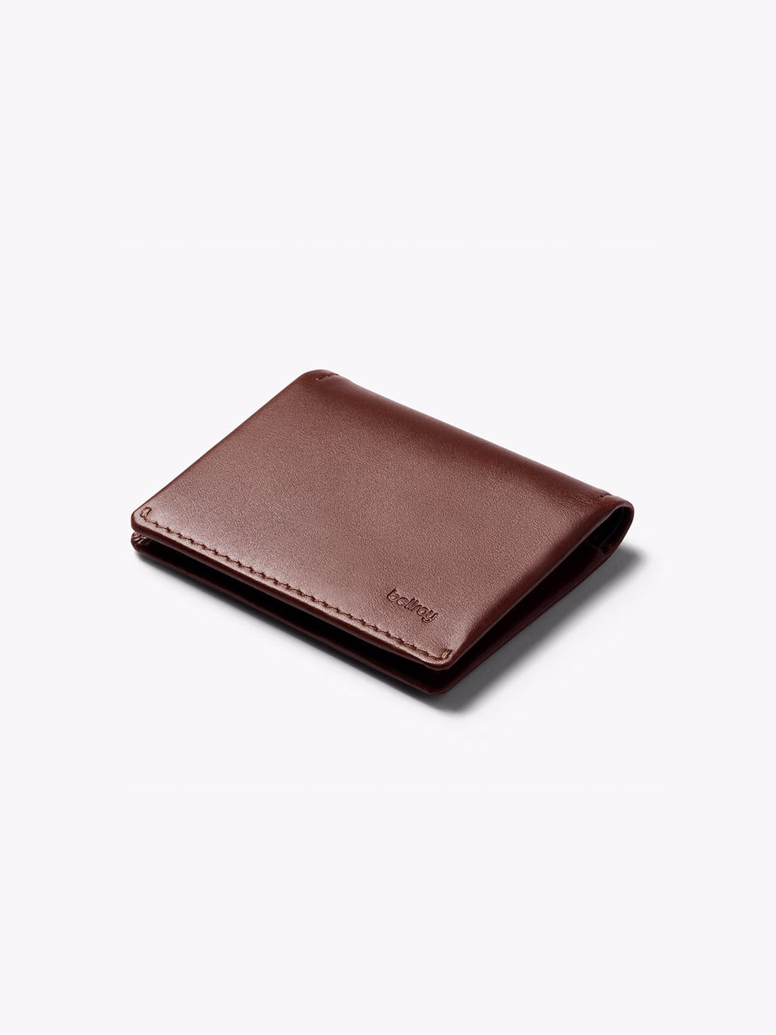 A closed Bellroy Slim Sleeve Wallet made of brown leather with neat stitching lies on a white surface. The minimalist wallet features an embossed “Bellroy” logo in the lower right corner.