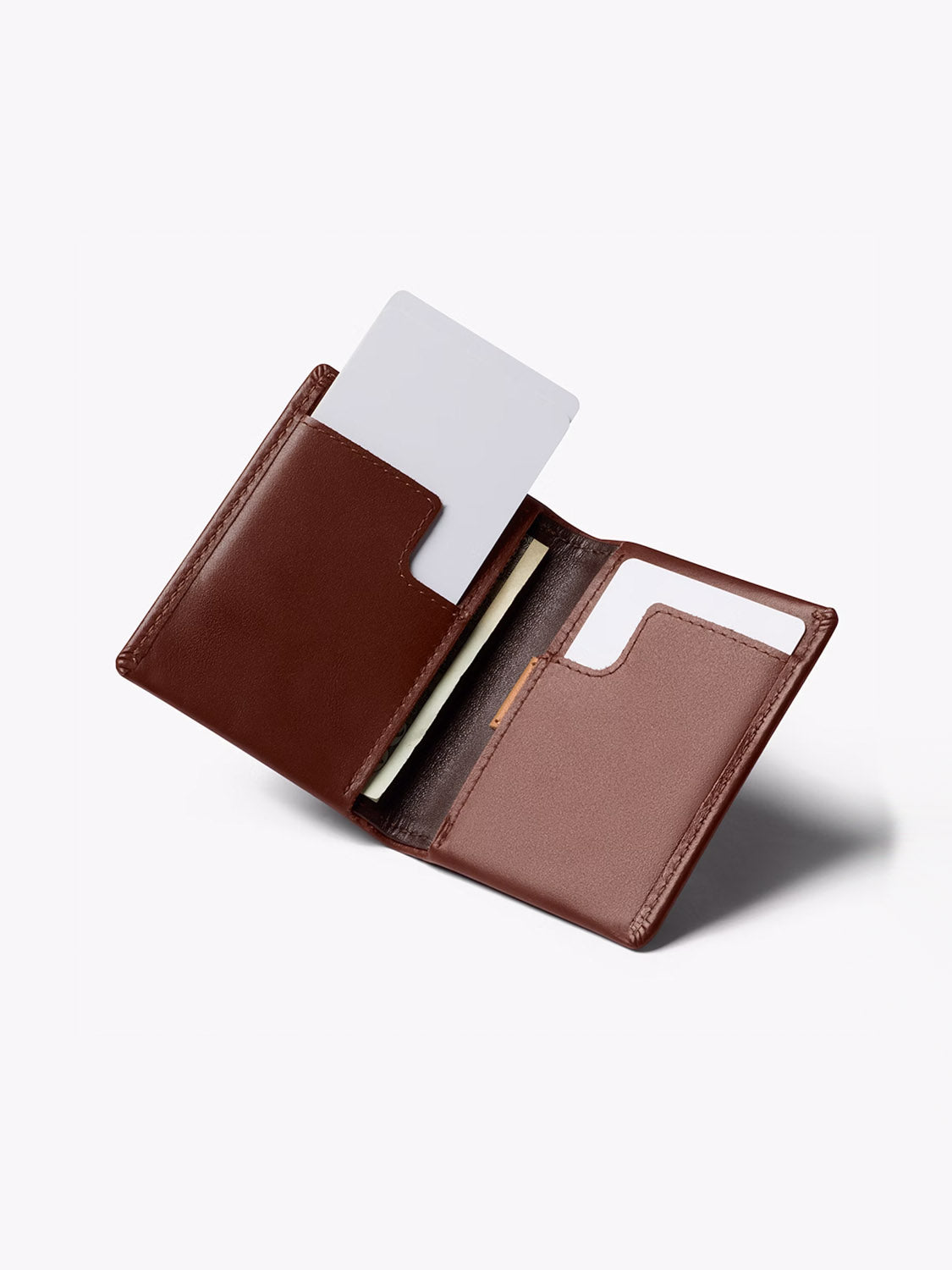 The Bellroy Slim Sleeve Wallet, in brown leather, is open on a plain light background, showing a card partially inserted in one slot and another visible slot on the opposite side.