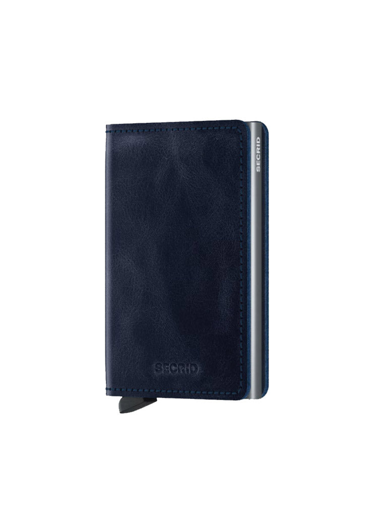 The Secrid Slimwallet Vintage Leather is a navy blue leather wallet with RFID/NFC protection, metallic accent, and SECRID branding. A black tab extends from the bottom as it stands upright against a white background.