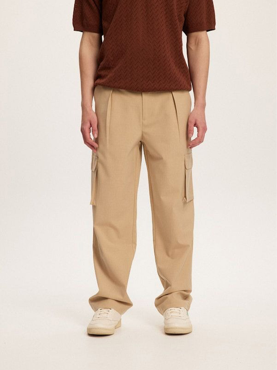A person showcases a versatile style in a brown patterned shirt paired with Kuwallas Smart Cargo Pants, featuring a tailored fit and convenient pockets, against a plain background. Light-colored shoes complete the look.