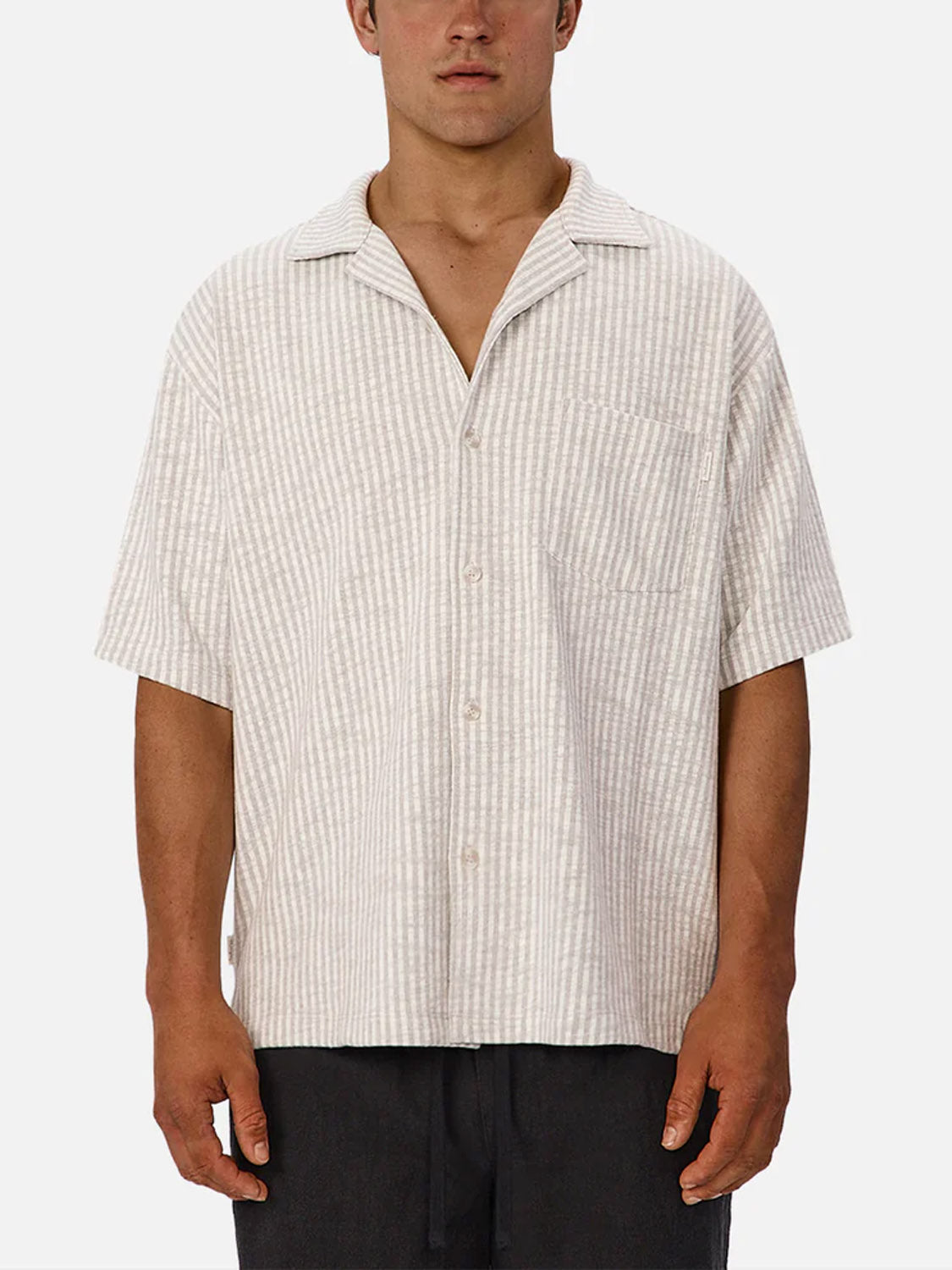 A man wears the Industrie Sonora Short Sleeve Shirt—a light beige and white striped, breathable cotton shirt with a collar and chest pocket—standing against a plain white background.