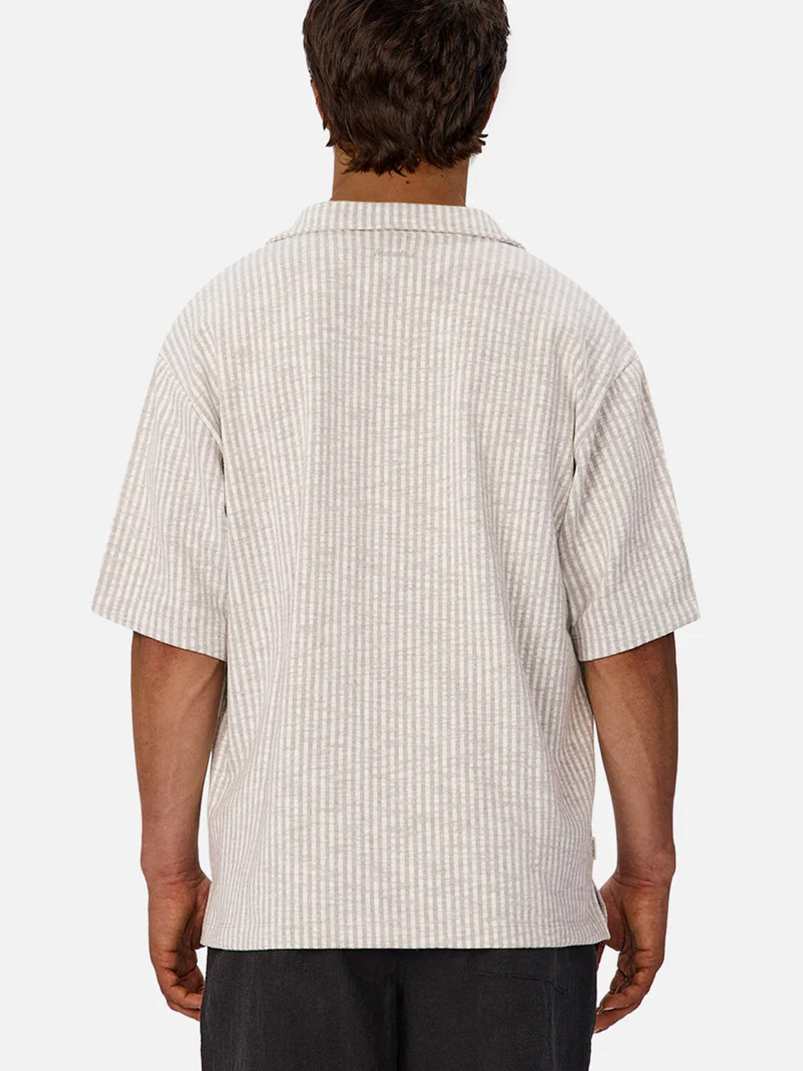 A person is seen from behind wearing the Sonora Short Sleeve Shirt by Industrie, featuring light-colored vertical stripes and dark pants. The breathable cotton shirt stands out against a plain white background.