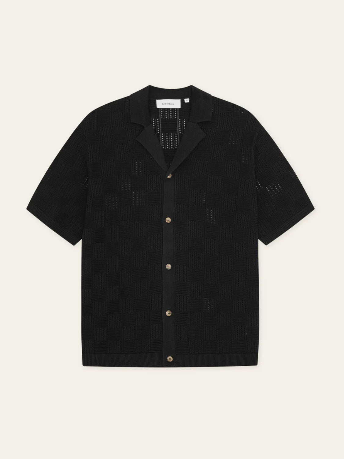 The Les Deux Squared Knitted SS Shirt is a black cotton short-sleeve shirt with a semi-sheer checkerboard texture, camp collar, and button-up front, shown laid flat on a light background.
